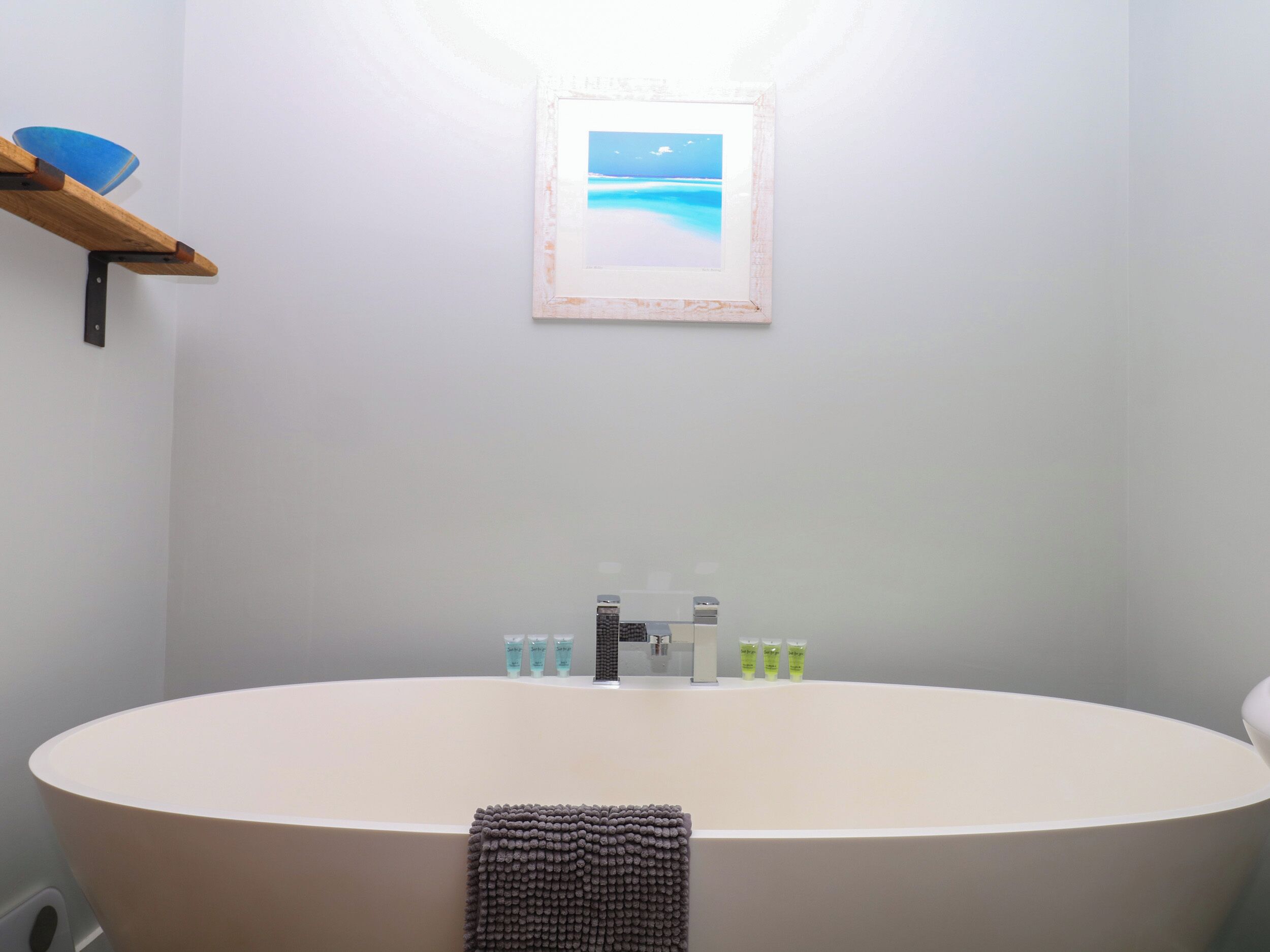 A bathroom with a large bathtub, a shelf with toiletries, and a framed picture on the wall.