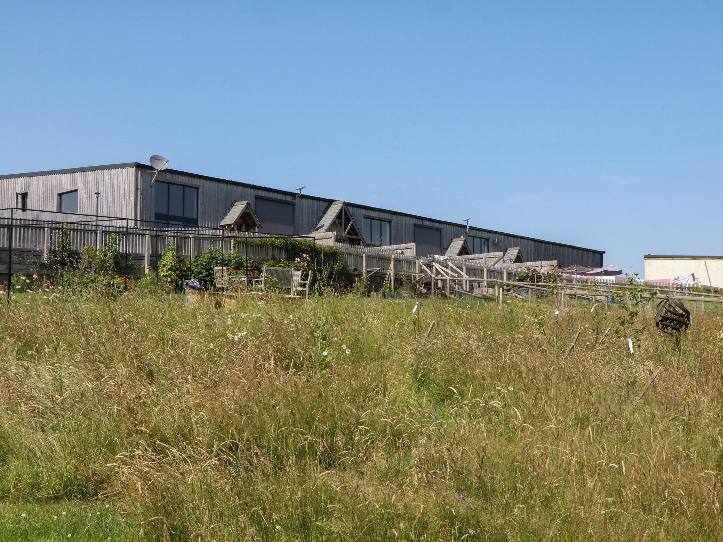 A large industrial building with multiple sections, surrounded by tall grass and a fence.