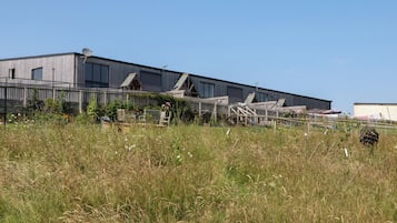 A large industrial building with multiple sections, surrounded by tall grass and a fence.