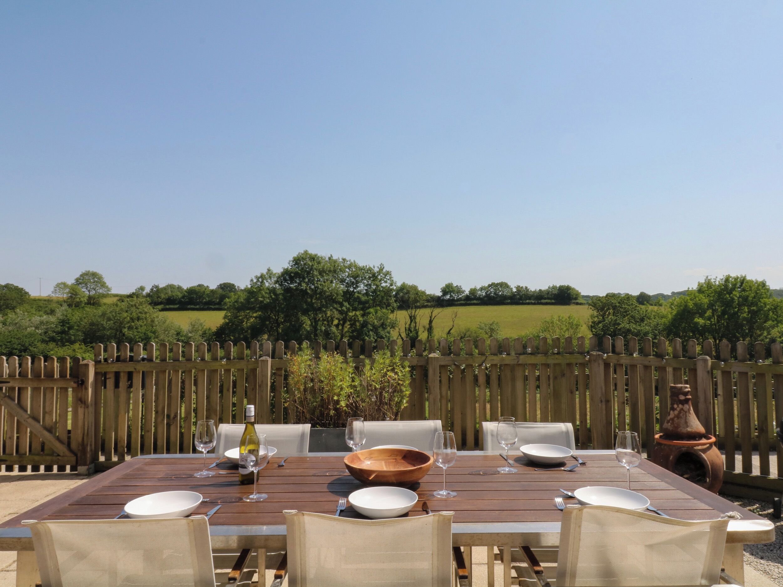 An outdoor dining table set with chairs, a wine bottle, and a terracotta pot.