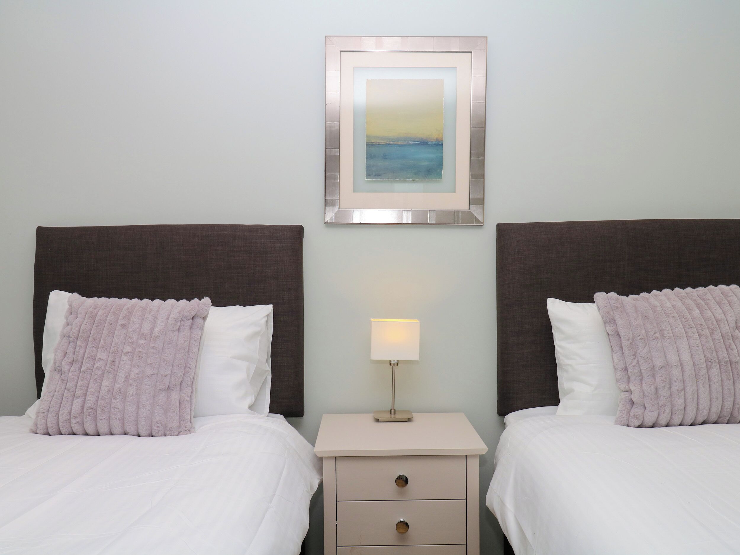 A hotel room with two beds, a nightstand with a lamp, and a framed picture on the wall.