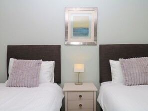 Una habitación de hotel con dos camas, una mesita de noche con lámpara y un cuadro enmarcado en la pared.