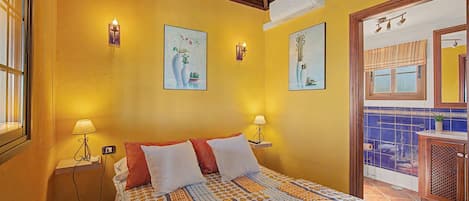 A hotel room with a bed, two bedside lamps, a wall-mounted air conditioner, and two framed artworks.