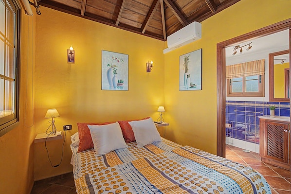 A hotel room with a bed, two bedside lamps, a wall-mounted air conditioner, and two framed artworks.