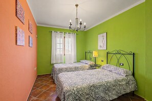 A room with two beds, a chandelier, a window with curtains, and artwork on the walls.