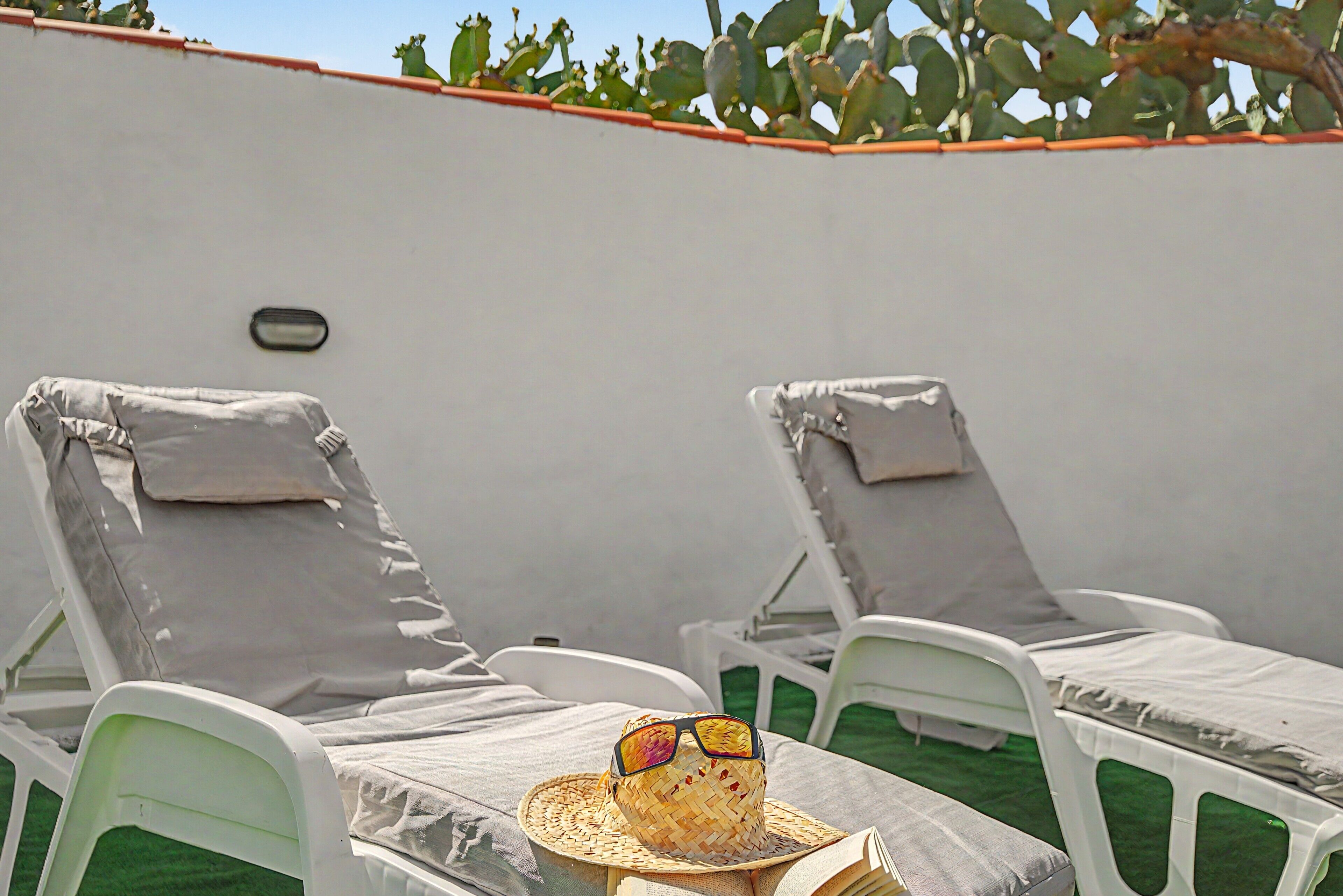 Two white lounge chairs with grey cushions, a woven hat, and sunglasses on a table.