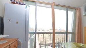 A balcony with a view of buildings, a refrigerator, a wooden dresser, and a table with a bowl.