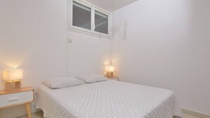 Un dormitori amb un llit, dues taules de nit amb làmpades, una finestra i una porta.