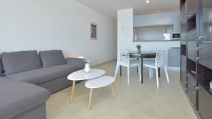 Un saló modern amb un sofà gris, una taula petita blanca i dues cadires blanques.