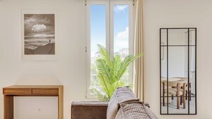 Una habitación con un escritorio de madera, un sofá, un ventanal con vistas a edificios y un cuadro en la pared.