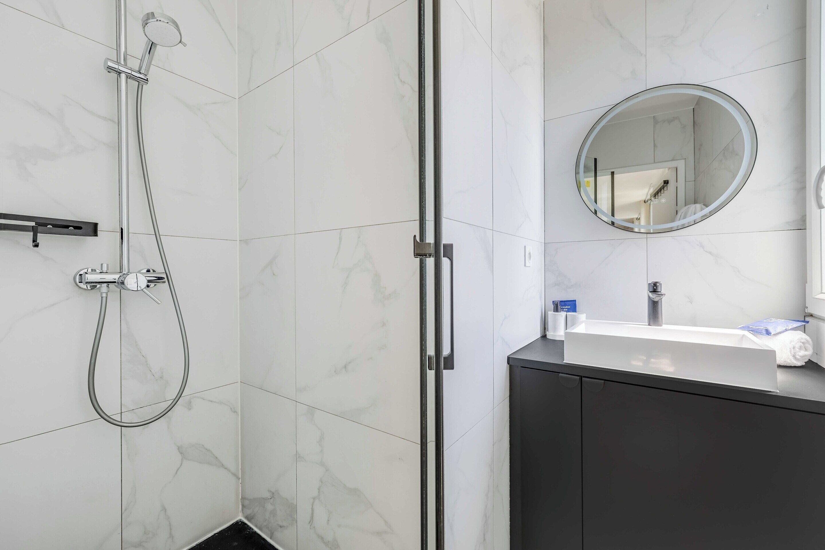 A bathroom with a shower, a sink, a mirror, and a dark cabinet.