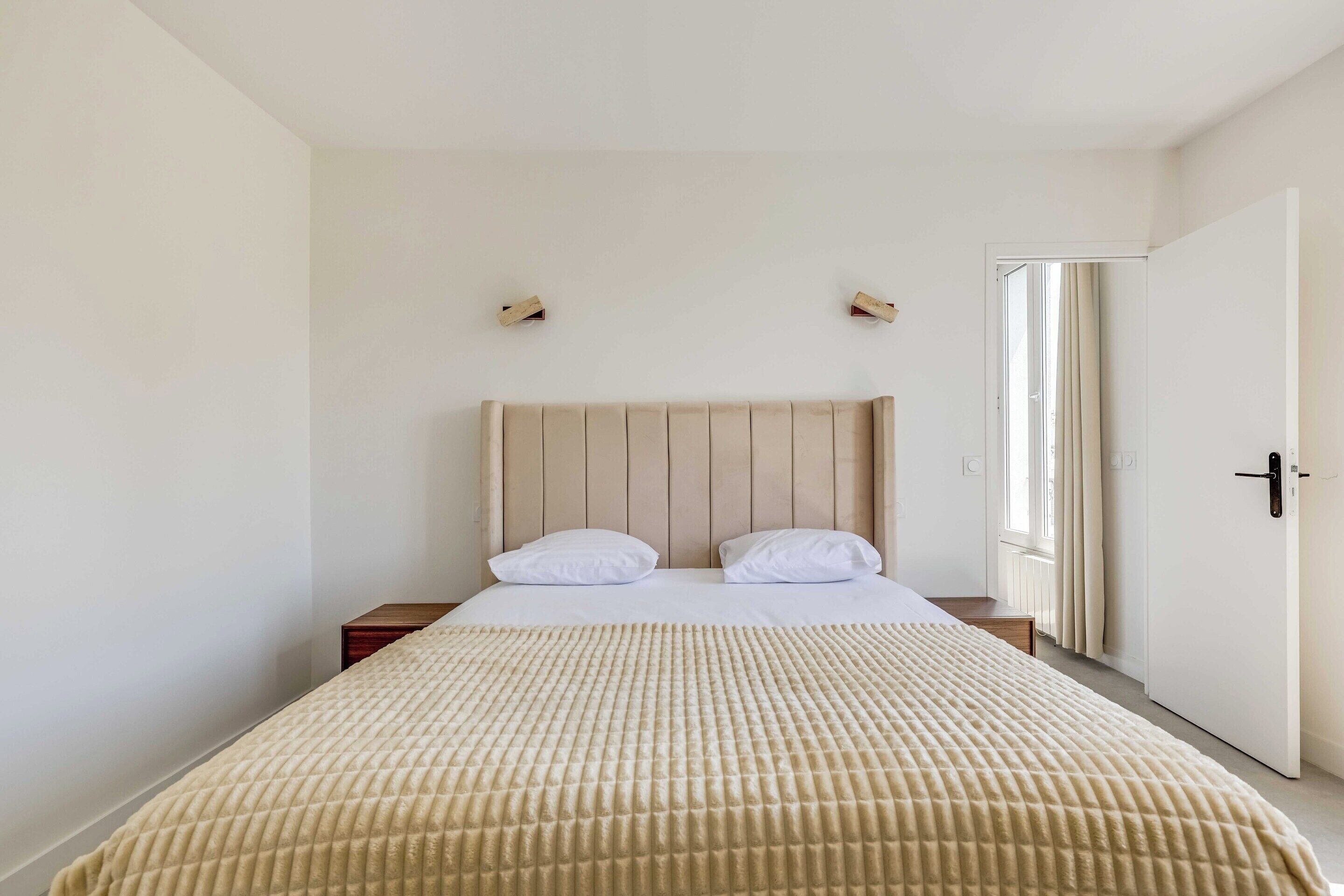 Ein Schlafzimmer mit einem Bett, zwei Nachttischen, einem Kopfteil und einer Tür zu einem anderen Raum.