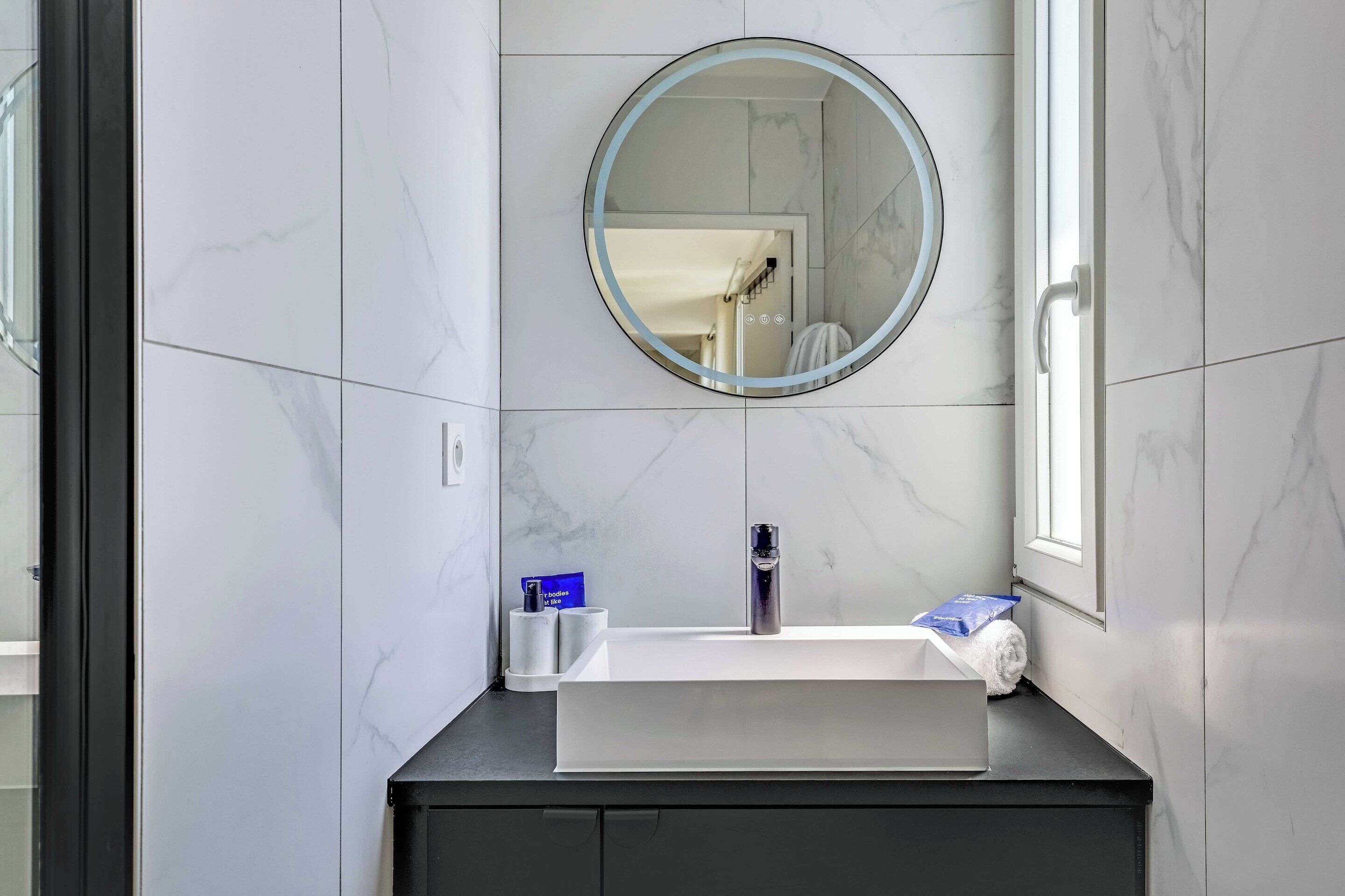 Een badkamer met een ronde spiegel, een witte wastafel en een handdoekhouder.