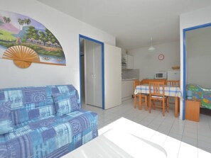 Ein Zimmer mit einem blauen, gemusterten Sofa, einem Esstisch mit Stühlen, einer Küchenzeile und einem Bett mit bunter Bettdecke.
