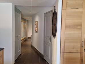 A hallway with a wooden cabinet, a door with a clock, and a painting on the wall. - Spacious apartment, panoramic view - 6 guests (Les Contamines-Montjoie)