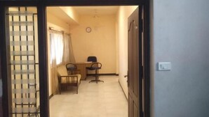 A service apartment entrance with a sign, a door, a window with curtains, and a small table with chairs.