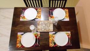 A dining table with four white plates, a central serving tray, and a fruit-patterned placemat.