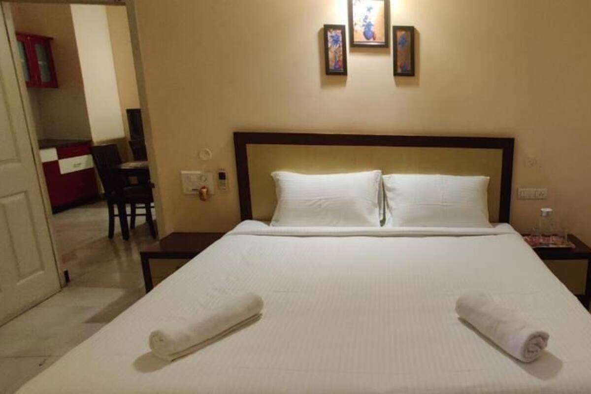 Habitación de hotel con una cama grande, dos almohadas, una mesita de noche, una lámpara de pared y una puerta que da a un baño.