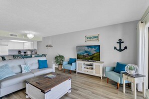 Ein modernes Wohnzimmer mit Sofa, Couchtisch, Fernseher und einer Küche im Hintergrund.