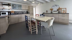 Eine moderne Küche mit hellen Holzschränken, einem weißen Esstisch und einer Decke mit freiliegenden Balken.