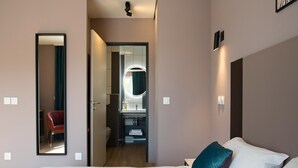 Una habitación de hotel moderna con una cama grande, un espejo, un baño pequeño y una puerta que da a otra habitación.