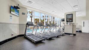 Ett gym med löpband, en pool och stora fönster med utsikt över palmer.