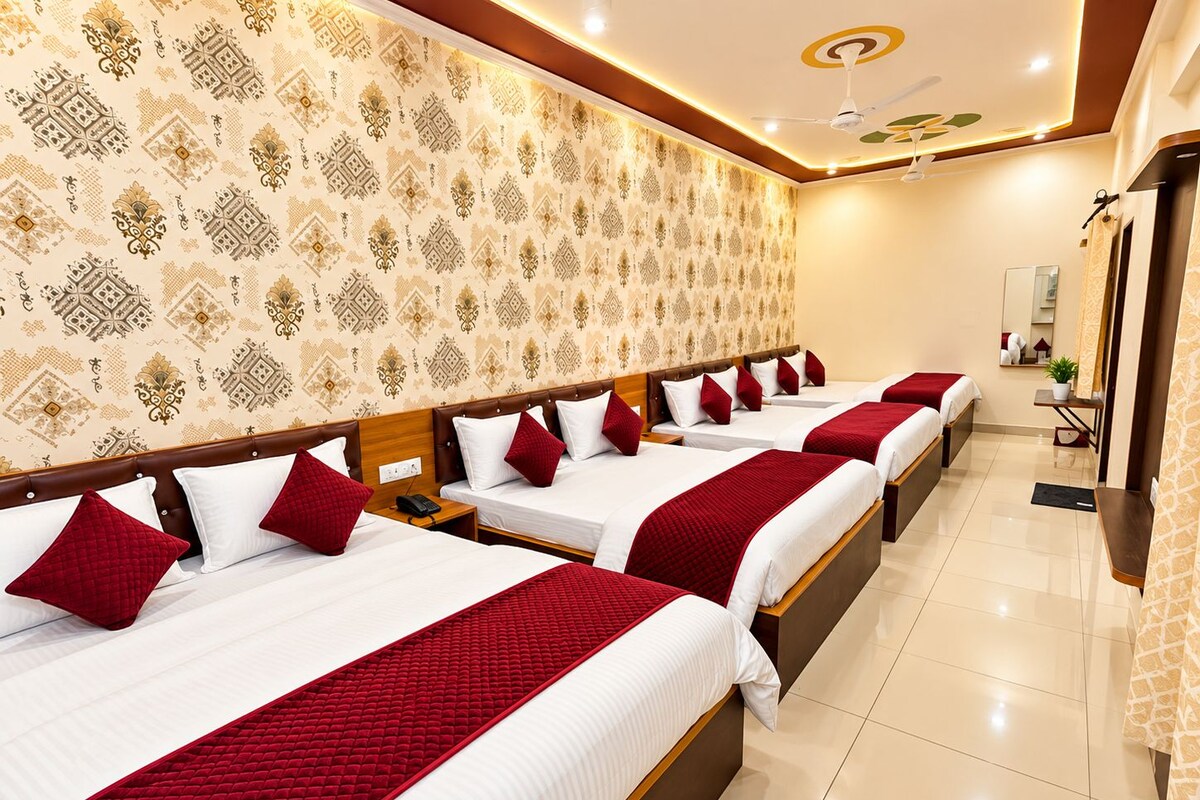 A hotel room with four beds arranged in a row, each with white bedding and red accents.