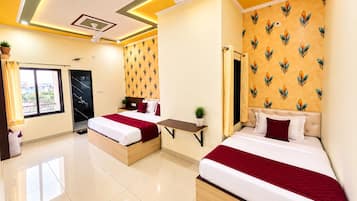 Quarto de hotel com duas camas, uma mesinha, um ventilador de teto e uma janela com cortinas.