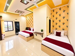 A hotel room with two beds, a small table, a ceiling fan, and a window with curtains. - Santosh Palace  (Danta Ramgarh)
