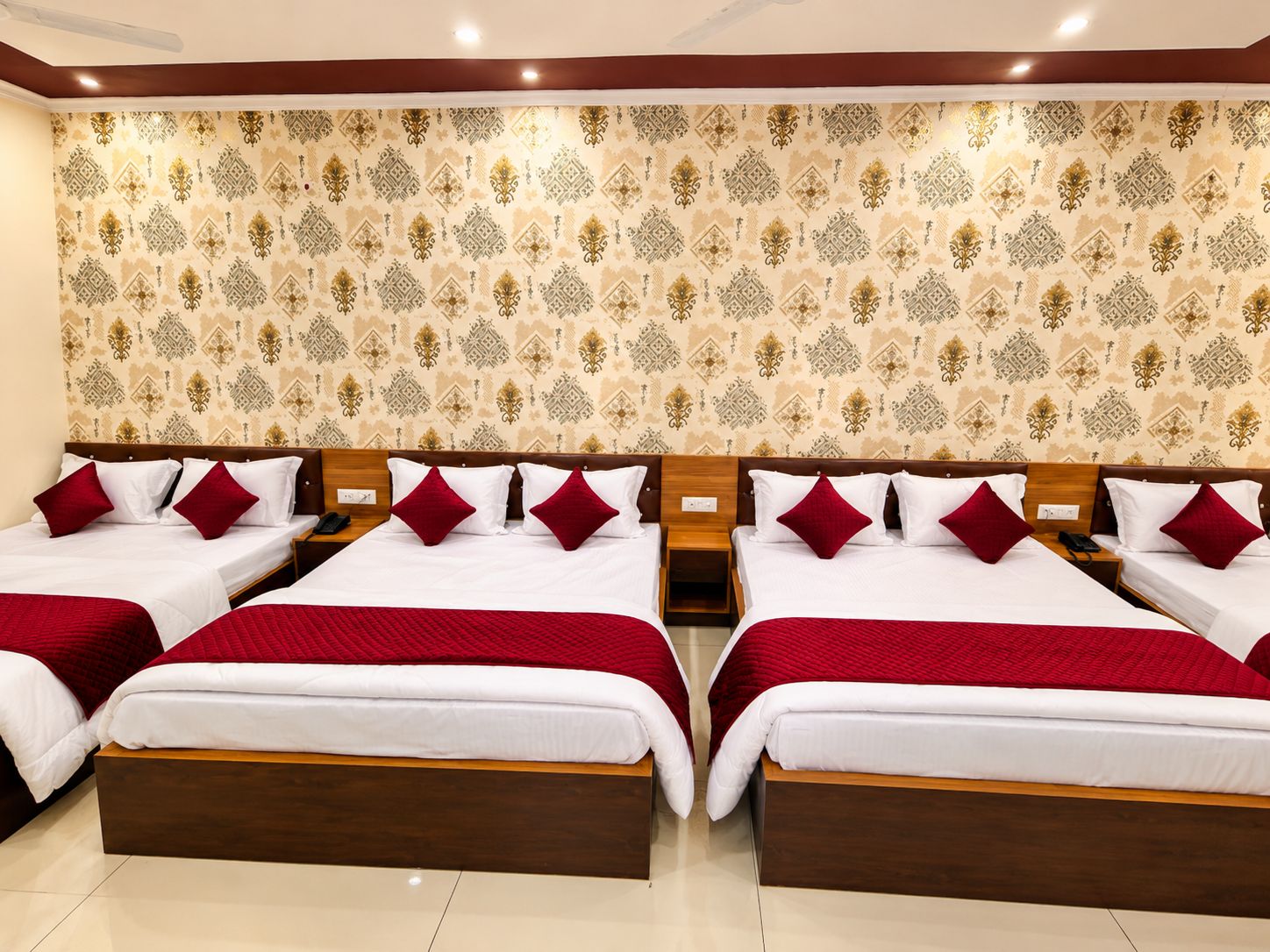 A hotel room with four beds arranged in a row, each with white bedding and red accents.