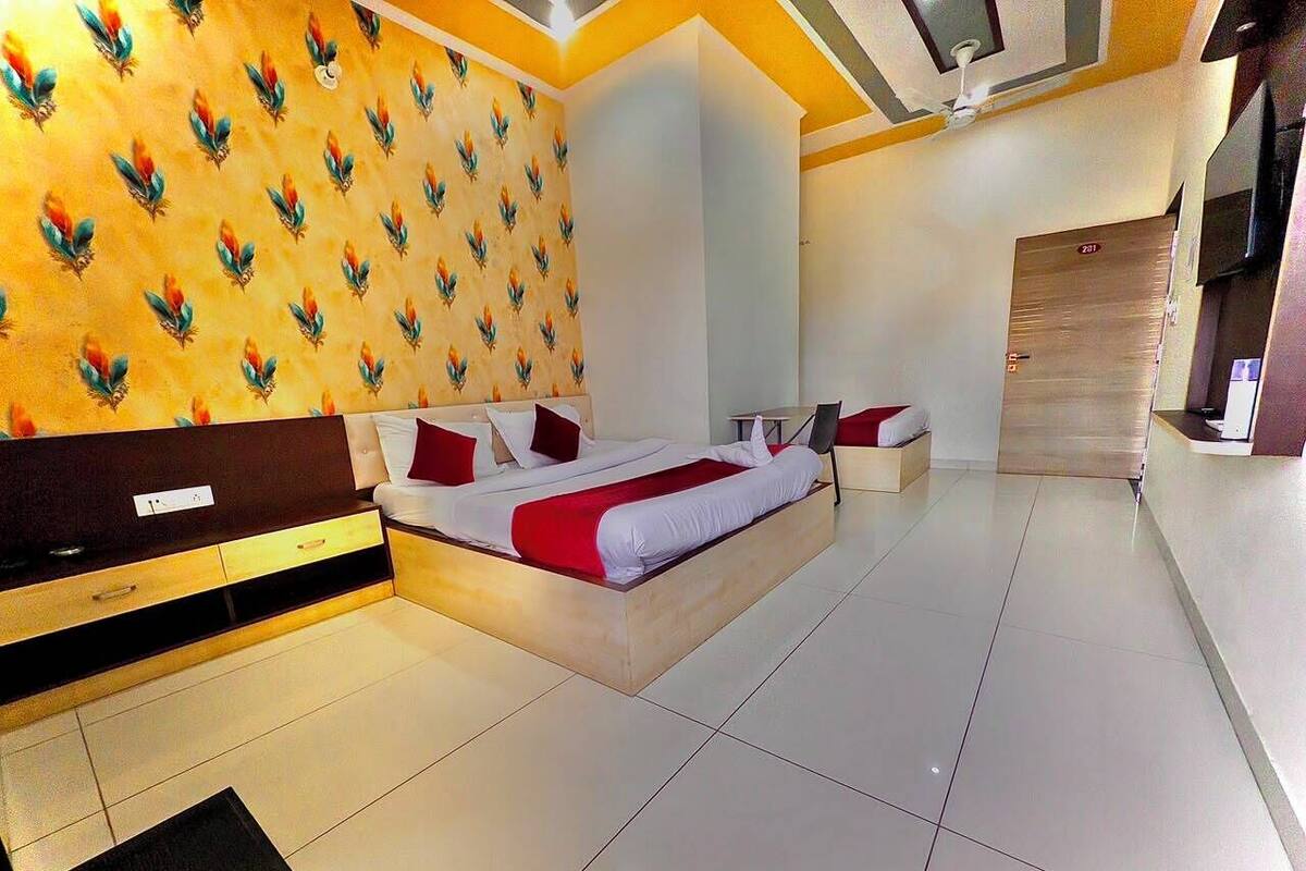 A modern hotel room with a large bed, a wooden headboard, a wall with a leaf pattern, a wardrobe, and a tiled floor.