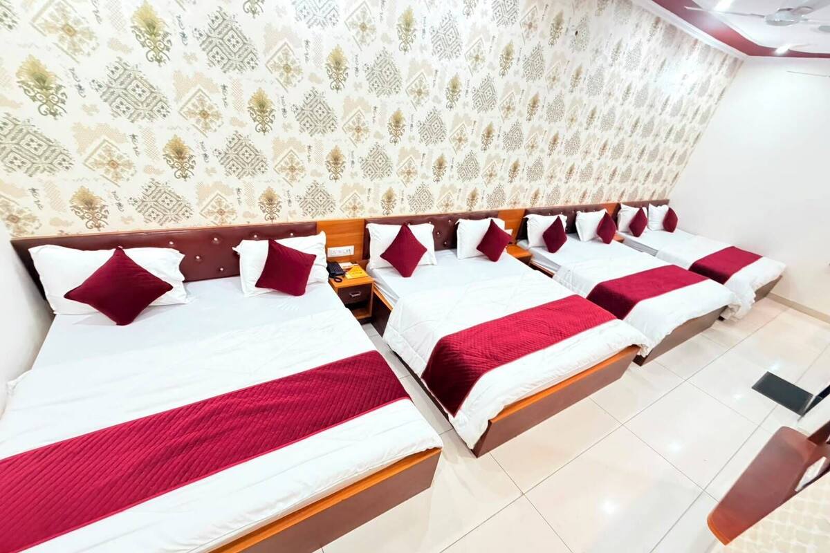A hotel room with six beds arranged in a row, each with white bedding and red accents.