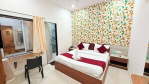 Habitación de hotel con cama, escritorio, silla, mesita de noche y ventana con cortinas.
