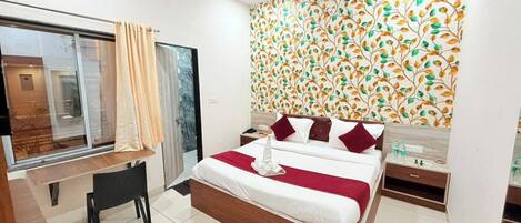 Habitación de hotel con cama, escritorio, silla, mesita de noche y ventana con cortinas.