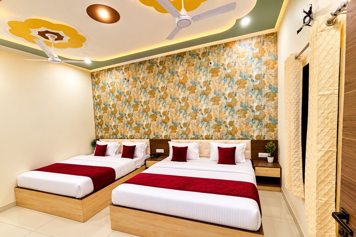 A hotel room with two beds, a ceiling fan, a floral wallpaper, and a wooden door.