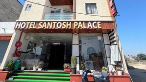 Un hotel de varios pisos llamado 'Hotel Santosh Palace', con un letrero llamativo, una escalera que lleva a la entrada y una moto estacionada.