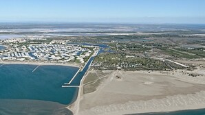 An aerial view of a coastal area with a marina, sandy beach, and residential buildings. - Studio 150m from the beach - 2 guests (Le Grau-du-Roi)