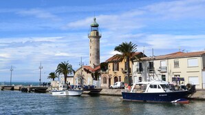 A coastal town with a lighthouse, boats docked at the pier, and buildings along the waterfront. - Studio 150m from the beach - 2 guests (Le Grau-du-Roi)