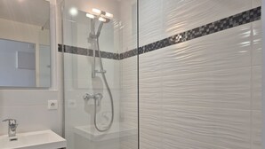 Uma casa de banho moderna com cabine de duche em vidro, lavatório branco e espelho.