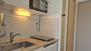 Uma cozinha compacta com micro-ondas embutido, pia de aço inoxidável e geladeira branca.