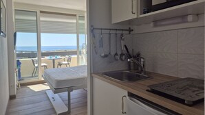 Cozinha compacta com pia, bancada e vista para o oceano através de uma porta deslizante.