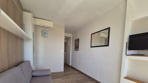 Uma sala moderna com um sofá, uma televisão de tela plana e um corredor que leva a outro espaço.