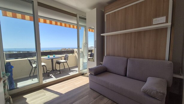 Varanda com mesa e cadeiras, um sofá e vista para o mar.