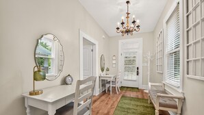 A room with a white desk, chair, and a mirror. There is a chandelier, a clock, and a window with blinds. - Tide Twins 1 | Sleeps 10 | Pet Friendly | 1.9 Miles to Bryant-Denny Stadium (Tuscaloosa)