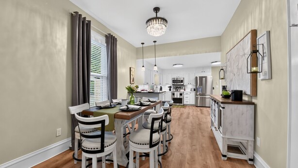 A dining area with a wooden table and chairs, a chandelier, and a kitchen in the background. - Tide Twins 1 | Sleeps 10 | Pet Friendly | 1.9 Miles to Bryant-Denny Stadium (Tuscaloosa)