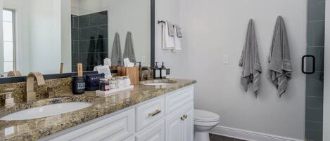 A bathroom with a large mirror, two sinks, a toilet, and towels on the wall.