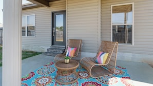 Eine Veranda mit zwei Korbstühlen, einem kleinen runden Tisch und einem bunten Teppich.