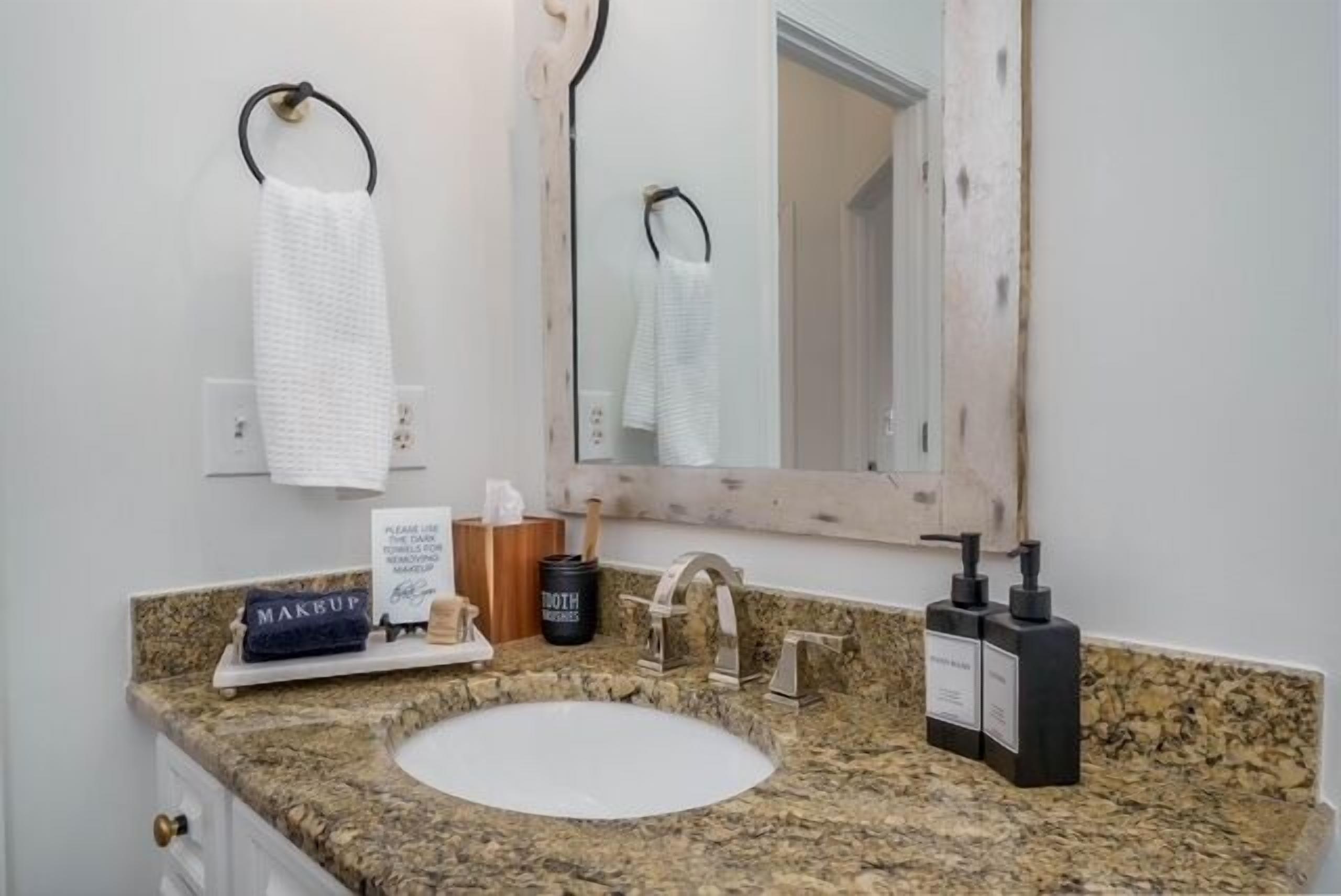 A bathroom with a granite countertop, a white sink, a mirror, a towel rack, and toiletries.