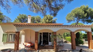 Una villa con techo de tejas, un porche cubierto, mobiliario exterior y un ventanal grande.