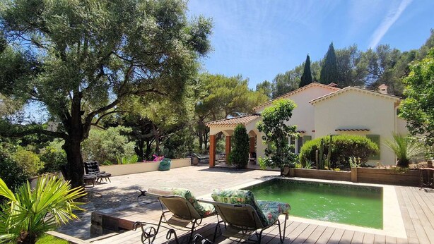 Zona junto a la piscina con sillones de descanso, una pérgola y un edificio con tejado de azulejos.